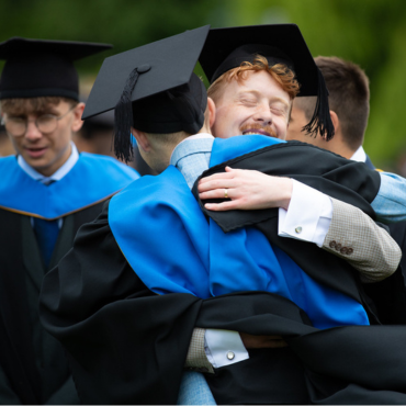 Two UCD graduates hugging, wearing graduation caps and gowns.